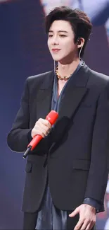 Performer in dark suit with red microphone on stage.