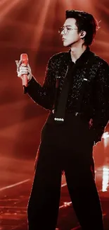 Stylish performer in elegant black outfit under red stage lights.