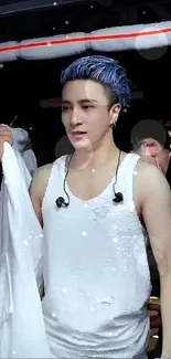 Performer with blue hair in white attire backstage, vibrant scene.