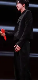 Performer in black with red microphone on stage.