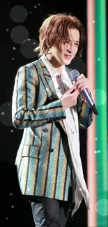 Performer wearing a stylish striped blazer on stage with dark teal background.