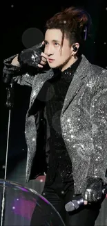 Performer in silver sequin jacket on stage with microphone.