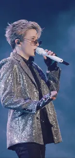 Stylish performer on stage in sequin jacket and sunglasses, holding a microphone.