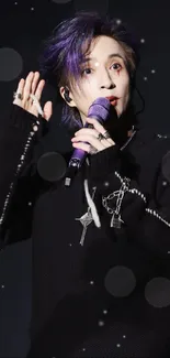 Performer in black outfit with purple hair holding a microphone on stage.