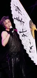 Performer in black attire with artistic fan on stage.