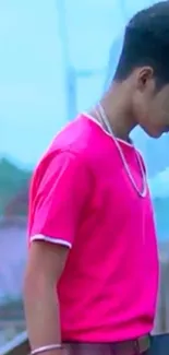 Person wearing a vibrant pink shirt standing on a bridge.