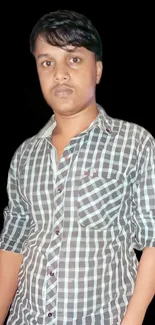 Portrait of a young man in a plaid shirt on a dark background.