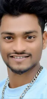 Portrait of a smiling person wearing a light blue shirt and chain.