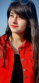 Woman in red jacket with sunglasses posing outdoors.