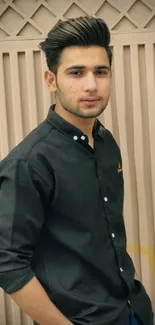 Portrait of a stylish young man in a black shirt standing against a beige background.