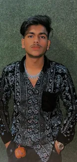 Stylish young man in a black patterned shirt against a dark green background.