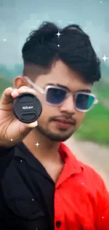 Young man holding camera lens on railway track wearing sunglasses.