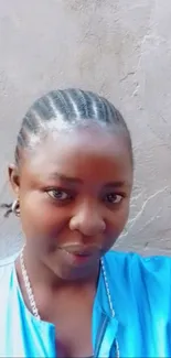 Woman with braided hair against a textured wall, wearing a blue top.