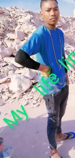 Man in blue shirt standing against rocky background, vibrant and stylish.