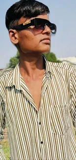 Portrait of person in sunglasses with striped shirt outdoors.