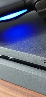 PS4 console with controller and blue light glow on wooden surface.