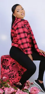 Woman in red checkered shirt seated, with pink floral decor.