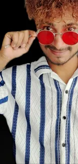 Portrait of person with red glasses and striped shirt on a black background.