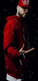 Person in a red hoodie, shadowed in rain on black background.