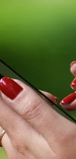 Close-up of stylish red nails holding a smartphone with green background.