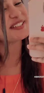 Woman taking a selfie with red-cased phone, smiling vibrantly.