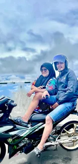 Two people on a motorcycle with a scenic cloudy background.