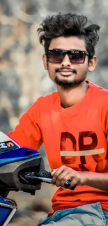 Young man in orange sweater on a blue motorcycle.