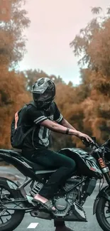 A biker rides on a road with orange autumn foliage around him.