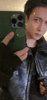 Stylish individual in dark leather jacket taking a selfie with phone.