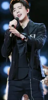 Charismatic singer in black suit on stage, vibrant background.