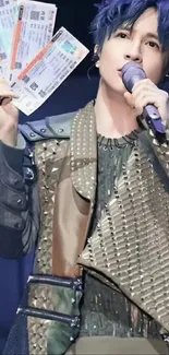 Singer on stage holding concert tickets, wearing stylish outfit.