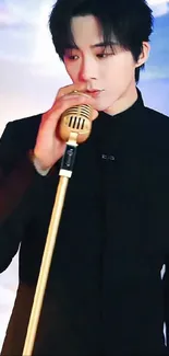 Singer in black outfit with gold microphone on stage.