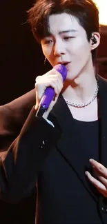 Singer in black suit with purple mic on stage.