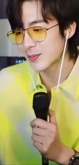 Singer holding a microphone wearing neon yellow shirt and shades.