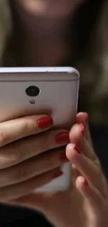 Close-up of a smartphone held with red-nailed hands.