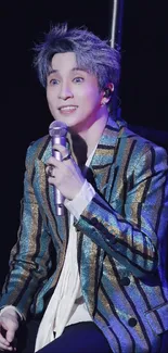 Stylish performer with shimmering outfit on stage, holding a microphone.