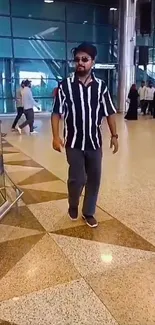 Man in striped shirt at a sleek, modern shopping mall.