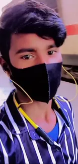 Stylish young person in a black mask and striped shirt at a train station.