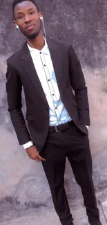 Man in black suit standing against a textured wall.