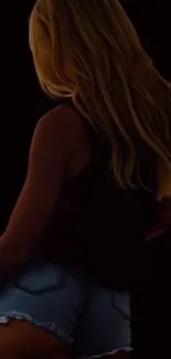 Silhouette of a woman in denim shorts on a dark background.