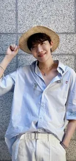 Person in straw hat and light blue shirt against a grey wall.