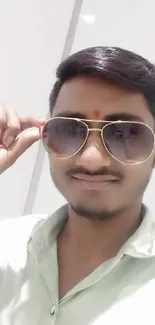 A stylish man wearing sunglasses with a beige background.