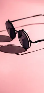 Round sunglasses casting shadow on pink background.