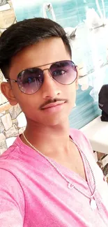 Selfie of a young man in sunglasses and a pink shirt in a stylish setting.