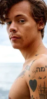 Man with tattoos at the beach, ocean backdrop.