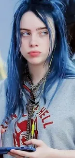 Teen with blue hair holding phone in a casual outfit.