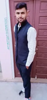 Man in traditional attire stands confidently by a wooden door.