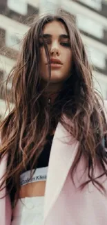 Woman with flowing hair in urban setting wearing light pink jacket.