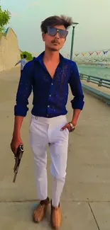 Man in blue shirt and white pants posing by a riverside walkway.