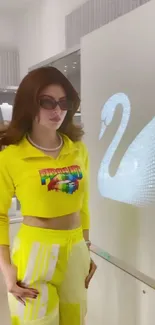 Stylish woman in yellow outfit with sunglasses, swan art in background.